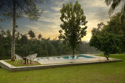 a swimming pool with two chairs and a tree at Theeram Riverside Holiday Home in Māla