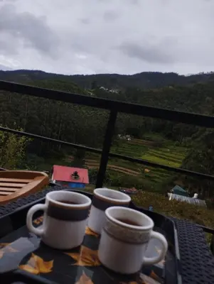 two cups on a table with a view of the mountains at Hazy Mount Vattavada in Kottakamboor