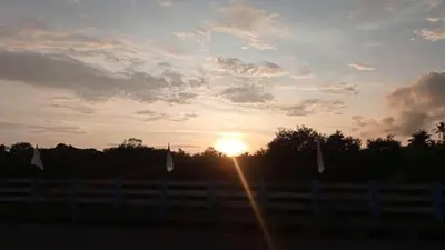 a sunset over a fence with the sun in the sky at Shruthi's Aarohi-Nature's Retreat Homestay in Kannur
