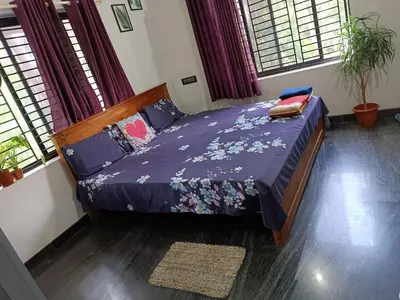 a bedroom with a bed with purple sheets and windows at Shruthi's Aarohi-Nature's Retreat Homestay in Kannur