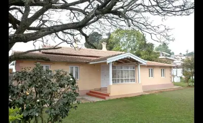 a small yellow house with a tree in front of it at Bella Vista Homestay in Coonoor