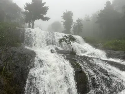 a waterfall on the side of a mountain in the fog at Brooke hills falls view in Vallikavungal