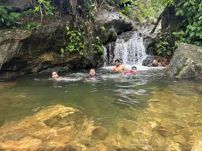 three people swimming in the water near a waterfall at Brooke hills 2 BHK villa falls view in Vallikavungal