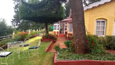 a yellow house with chairs and a tree in the yard at Wyoming Heritage in Ooty