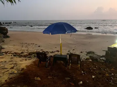 a table and two chairs under an umbrella on the beach at Rocks beach house in Kannur