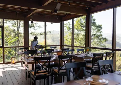 a man standing in a restaurant with tables and chairs at LohonoStays Villa Amani 8B in Coonoor