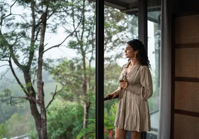 a woman in a dress looking out of a window at LohonoStays Amani Villa 10A in Coonoor