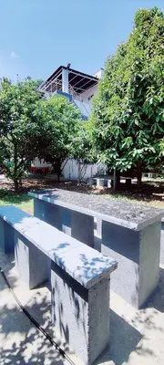 a concrete bench in a park with trees and a building at Nature stay Mysore in Mandya