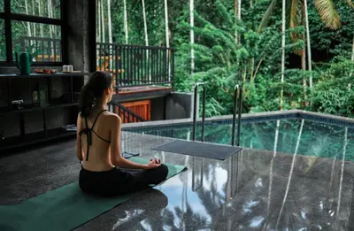 a woman sitting on the floor next to a pool at Bhadra - The Estate Villa in Wayanad