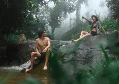 a man and a woman sitting on a rock in the water at Bhadra - The Estate Villa in Wayanad