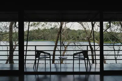 two chairs and a table in front of a river at Lakedale Resorts in Thekkumkara