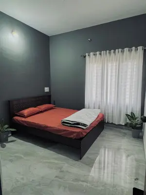 a bedroom with a bed with red sheets and white curtains at Stayover Homestay in Mysore