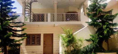 a white house with a balcony and trees at GEM Stays in Ooty