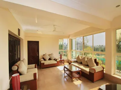 a living room with two couches and windows at Bota Royal in Kushālnagar