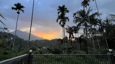 a sunset with palm trees and mountains in the background at Hill View Heights Wayanad in Meppādi