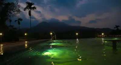 an empty swimming pool at night with green lights at Mountain Wings Resort in Vythiri