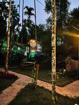 a garden with a house with lights in the background at Josh Holidays Wayanad in Vaduvanchal