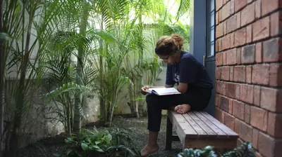a woman sitting on a bench reading a book at Vettaths in Kozhikode