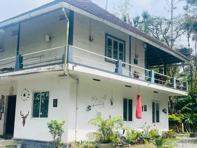 a white house with a balcony on top of it at LAKSHMI NIKUNj Estate Stay in Madikeri