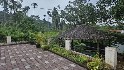 a pavilion with a straw roof next to a walkway at Happydays Hut in Mananthavady