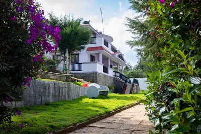 a white house with a stone wall and flowers at Haven inn in Kotagiri