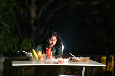 a woman sitting at a table with a bowl of fruit at Ayurnest Pool Resort Wayanad in Batheri