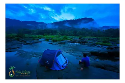 a person sitting next to a tent next to a river at Holy Village Homestay in Neriyamangalam