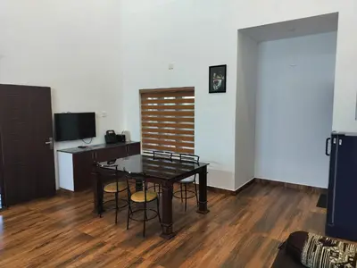 a dining room with a table and chairs and a desk at Roneys Villa in Wayanad
