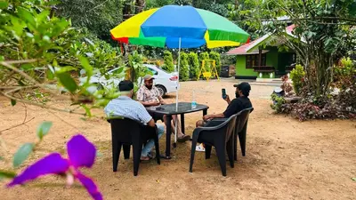 a group of people sitting at a table under an umbrella at Golden pearl private villa with pool in Vythiri