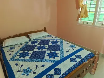 a bed with a blue and white quilt on it at Abiraksha Stay Coorg in Madikeri