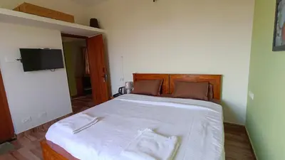 a bedroom with a large bed with white sheets and a television at Dwarka Home Stay in Ooty