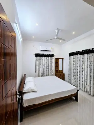 a bedroom with a bed with white sheets and curtains at Mariya Home Stay in Kanjikode