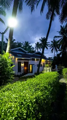 a house on the beach at night with palm trees at Sakthi River Resort in Pollāchi