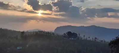 a sunset over a hill with trees and mountains at Dam Valley Home Stay Resort in Parambikolam