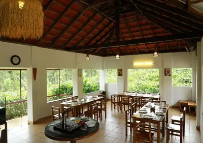 a dining room with tables and chairs and windows at Dhanagiri Homestay Wayanad in Vythiri