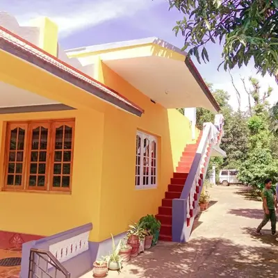 a man walking in front of a yellow house at Aghasthyashrya Homestay in Siddapur