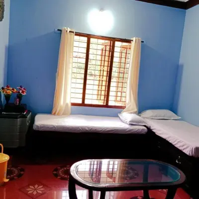 a room with two beds and a table and a window at Aghasthyashrya Homestay in Siddapur