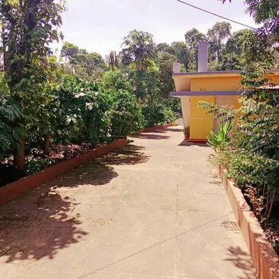 a sidewalk next to a yellow building with trees at Aghasthyashrya Homestay in Siddapur
