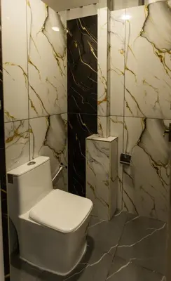 a bathroom with a white toilet and marble walls at Bharath Pods in Coimbatore