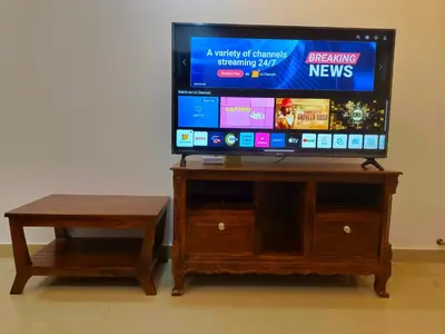 a flat screen tv on a wooden stand with a table at Posh 1 BHK Apt with Temple View in Guruvayur B1001 in Guruvāyūr