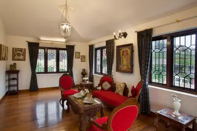 a living room with red chairs and a table and windows at Away From Home - 2 - Rooms In Ooty, Home Stay Ooty in Ooty
