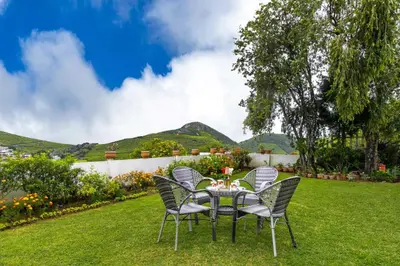 a table and chairs on a lawn with mountains in the background at Away From Home - 2 - Rooms In Ooty, Home Stay Ooty in Ooty