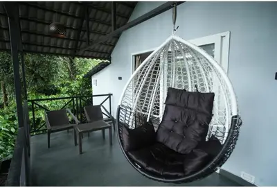 a hanging hammock with a chair on a porch at The Cozy Clouds Hill Saty in Madikeri