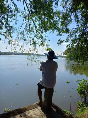 a man sitting on a rock looking at a lake at Green Haven Homestay in Kodungallūr