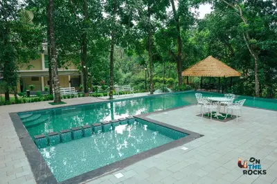 a swimming pool with a table and chairs next to at Athirapilly Ontherocks in Athirappilly