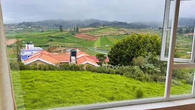 a window with a view of a green field at Away From Home - 3 - HomeStay Ooty, Entire 3BHK Villa in Ooty