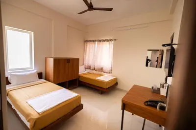 a bedroom with two beds and a desk and a window at Viba Residency in Coimbatore