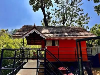 a red house with a roof on a platform at Little Bricks Reverside Private Pool Villa by GreenEscapes in Vythiri