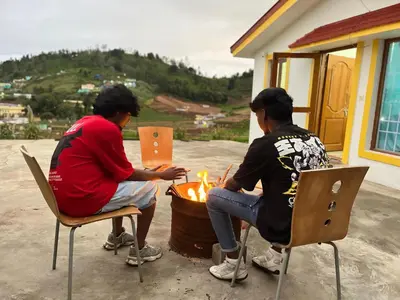 two men are sitting around a fire pit at Chillz Heaven Resorts - Ketti Palada in Coonoor