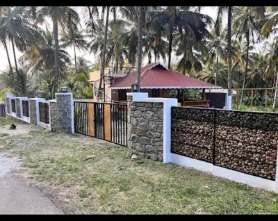 a stone fence in front of a house with palm trees at Mountain river farm resort in Agali